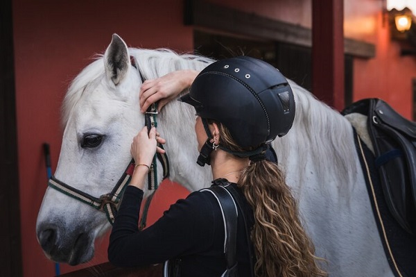 Comment choisir un casque d’équitation ? femme avec casque préparer cheval 