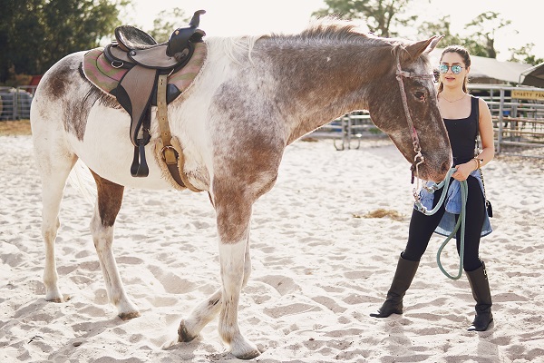 Peut-on monter à cheval quand on a ses règles, fille avec des lunettes de soleil marchant dans une ferme avec des chevaux