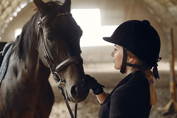 Quand dois-je changer mon casque d'équitation? Femme près d'un cheval. Cavalier en uniforme noir