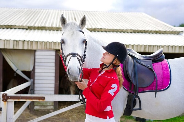 fille-cavalier-equestre-debout-pres-cheval-blanc-dans-ecurie-Comment entretenir sa tenue d'équitation?